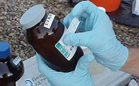 rubber gloved hands putting label on sample bottle